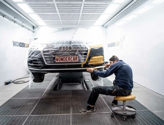 Réparateur Wondercar qui prépare la zone à réparer d'un pare-chocs d'une Audi noire dans la Smart box